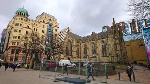 Leeds, İngiltere - 2.2.2.2018: Salgından önce bulutlu bir gökyüzünün altında Park Row 'daki Victorian Mill Hill Şapeli' nin önünden geçen yayaların yan görüntüsü
