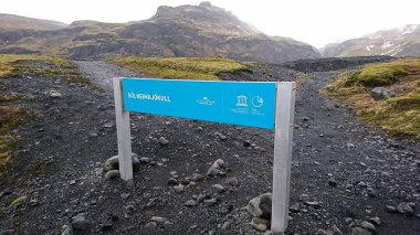 Solheimajokull, İzlanda - 3.26.2018: Solheimajokull Buzulu 'nun girişinde turistler olmadan sisli bir gökyüzünün altında kayalık dağlar, toprak yollar ve çimenler arasında bir işaret