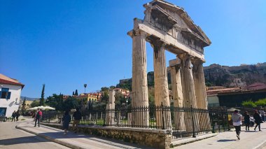 Atina, Yunanistan - 29,3,2018: Roma Agora 'nın girişi olan Athena Archegetis Kapısı' nın etrafında yürüyen turistler, Akropolis tepesinin arkasında salgından önce açık mavi bir gökyüzünün altında güneş ışığıyla birlikte