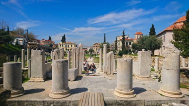 Atina, Yunanistan - 30.3.2018: Roma Agora 'da kırılan sütunlar arasında yürüyen turistler, salgından önce güneşli mavi gökyüzünün altında Athena Archegets' in kapısının arkasında yürüyorlar