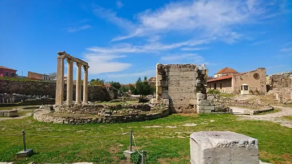 Atina, Yunanistan - 30.3.2018: Roma Agora 'da kışın hiç turist bulunmayan salgından önce güneşli mavi gökyüzünün altındaki çimlerin arasında ayakta duran sütunlar ve kırık duvarlar