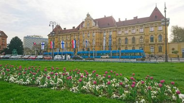 Zagreb, Hırvatistan - 11 Nisan 2018: Arka planda Muzej za umjetnost i obrt ve mavi tramvay ile birlikte ön planda renkli laleler çiçek açarak Zagreb 'deki kentsel ilkbaharın güzelliğini gözler önüne serdi