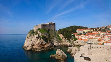 Dubrovnik, Hırvatistan - 14 Nisan 2018: Fort Lovrijenac 'ın berrak mavi Adriyatik Denizi ve eski şehrin güneş ışığı altındaki tarihi kiremitli çatılarına bakan kayalık bir çıkıntıya çarpıcı bir manzarası
