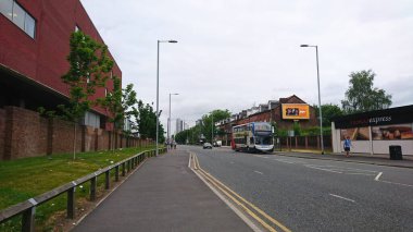 Manchester, İngiltere - 18 Haziran 2018: Sakin şehir sokak sahnesi, bulutlu bir günde yayalar ve şehir yaşamını ve toplu taşımayı ön plana çıkaran çift katlı bir otobüsü gösteriyor