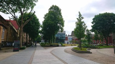 Manchester, İngiltere - 18 Haziran 2018: Manchester Üniversitesi kampüsündeki yaya yolunda yürüyen öğrenciler, bulutlu bir gökyüzü altında tarihi ve modern binalar ve ağaçlarla çevrili