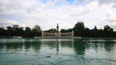 Madrid, İspanya - 28 Mayıs 2018: Retiro Park 'taki gölün kıyısındaki Kristal Saray manzarası, yeşillik ve ziyaretçilerle çevrili ve yazın sakin atmosferin tadını çıkaran bir ördek