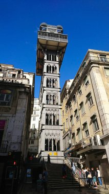 Lizbon, Portekiz - 1 Haziran 2018: İkonik Elevador de Santa Justa, açık mavi gökyüzünün altındaki canlı bir sokak sahnesinde, Neo-Gotik mimarisini sergileyerek yayaların üzerinde yükseldiği görüldü.