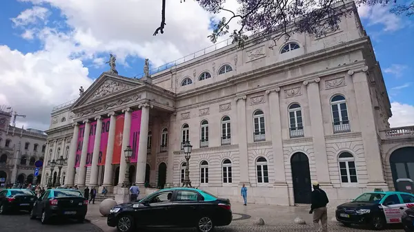 Lizbon, Portekiz - Haziran 12018: D. Maria Ulusal Tiyatrosu 'nun ihtişamı, önde park halindeki neoklasik cephesini uzun kolonlar, canlı tanıtım afişleri ve taksilerle sergiliyor.