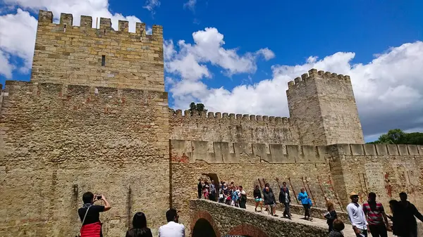 Lizbon, Portekiz - 1 Haziran 2018: Castelo de Sao Jorge 'nin antik duvarlarını keşfeden turistler, tüylü bulutlarla dolu açık mavi bir gökyüzü altında, bu tarihi yerde anıları yakalıyorlar.