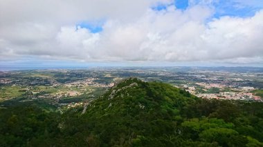 Sintra, Portekiz - 6.3.2018 Sintra dağlarının tepelerinden nefes kesici panoramik bir manzara Mağriplilerin Kalesi, yemyeşil tepeler ve parçalı bulutlu bir gökyüzü altında canlı bir manzara