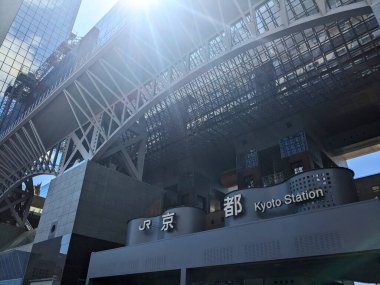 Kyoto, Japonya - 08.08.2024: JR Kyoto İstasyonu 'nun ana girişinin ön cephesi, tepeden gelen güneş ışığı ve modern eğimli tavan pencereli cam tavanın yanındaki güneş ışınları