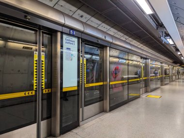 Londra, İngiltere - 2023.02.28: Southwark 'ta cam platform kapıları, seyahat bilgileri, yuvarlak logo ve yansımadan tren bekleyen yolcularla dolu neredeyse boş bir Jübile Hattı platformu