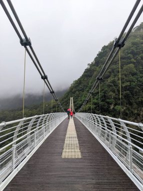 Taroko, Tayvan - 11.26.2022: Liwu Nehri üzerindeki simetrik Buluowan Kablo Askı Köprüsü üzerinde yürüyen turistler, salgın sırasında meydana gelen 403 depreminden önce dağlarda sisin olduğu yağmurlu bir günde