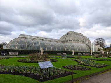 Londra, İngiltere - 02.26.2024: Kraliyet Botanik Bahçeleri 'ndeki Palm House cephesinin yan görünüşü Bulutlu bir gökyüzünün altında, önünde çiçeklerden ve çimlerden oluşan bir bahçeyle