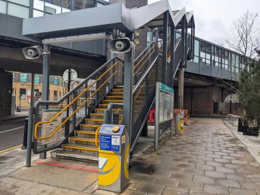 Londra, İngiltere - 2023.03.07: Köprüdeki platforma çıkan bir merdiven ve bulutlu bir günde bilet engeli olmayan iki sarı kart okuyucusu ile DLR Westferry İstasyonu girişi