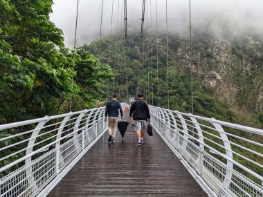 Taroko, Tayvan - 11.26.2022: Liwu Nehri üzerindeki Buluowan Kablo Askı Köprüsü üzerinde yürüyen turistler, yağmurlu bir günde salgın sırasında meydana gelen 403 depreminden önce dağlarda sis ile boğuşuyor.