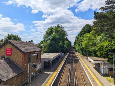 Meopham, İngiltere - 06.05.2024: Meopham İstasyonu 'nun istasyon binası ve her iki taraftaki platformların iki peronunda ağaçların yanında açık mavi gökyüzü ve güneş ışığı altında raylar var.