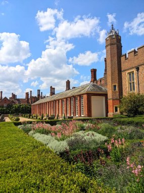 Londra, İngiltere - 07.19.2024: Hampton Court Palace 'daki Lower Orangery Garden' ın ön bahçesi ve güneş ışığı altındaki kırmızı tuğlalı binalardaki dekoratif Tudor tuğla bacaları