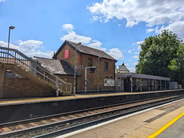 Meopham, İngiltere - 06.05.2024: Meopham İstasyonu 'nun istasyon binası ve platformun tepesinde önünde ağaçlar ve açık mavi gökyüzü ve güneş ışığı altında raylar bulunan bir bekleme alanı