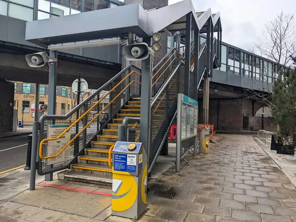 Londra, İngiltere - 2023.03.07: Köprüdeki platforma çıkan bir merdiven ve bulutlu bir günde bilet engeli olmayan iki sarı kart okuyucusu ile DLR Westferry İstasyonu girişi