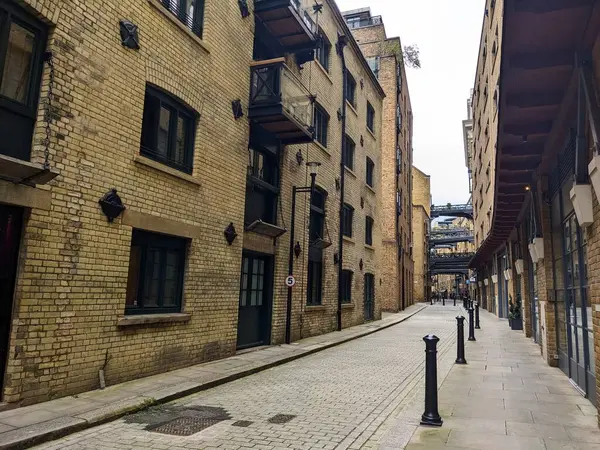 Londra, İngiltere - 05.13.2024: Shad Thames 'in sakin bir zamanı dönüştürülmüş depolarla ve fayanslı zemin üzerinde yükseltilmiş geçitlerle ve turistler olmadan bulutlu bir gökyüzünün altında zemin kattaki dükkanlarla