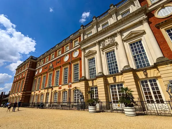 Londra, İngiltere - 07.19.2024: Kırmızı tuğla önünde yürüyen ve Hampton Court Palace 'da açık mavi gökyüzü altında güneşli bir yaz öğleden sonrasında Güney Cephesi' ni süsleyen ziyaretçiler