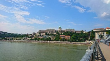 Budapeşte, Macaristan - 5 Haziran 2018: İkonik Buda Şatosu Tuna Nehri üzerinde Szechenyi Zinciri Köprüsü 'nün yanındaki parlak mavi gökyüzünün altında canlı şehir yaşamını gözler önüne sererek görkemli bir şekilde yükselir.