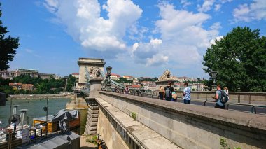 Budapeşte, Macaristan - 5 Haziran 2018: Tuna Nehri boyunca uzanan ikonik Zincir Köprüsü, turistlerin güneşli havanın ve güzel mimarinin tadını çıkararak geniş yürüyüş yolunda yürümeleri