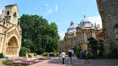 Budapeşte, Macaristan - 5 Haziran 2018: Vajdahunyad Şatosu 'nda, açık mavi gökyüzü altında gezinen ve çiçeklerin tadını çıkaran insanların yer aldığı güzel bir manzara