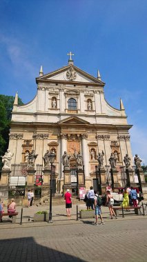 Krakow, Polonya - 9 Haziran 2018: Aziz Peter ve Paul Kilisesi 'nin görkemli cephesi, berrak mavi gökyüzü ve etrafı keşfeden ziyaretçiler arasında karmaşık heykellerle şaşırtıcı bir Barok mimarisi sergiliyor.