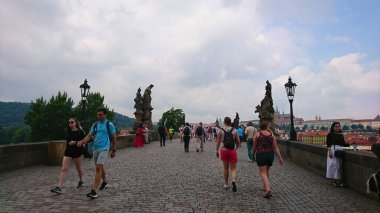 Prag, Çek Cumhuriyeti - 11 Haziran 2018: Ziyaretçiler, salgından önce bulutlu bir gökyüzü altında heykel ve canlı bir atmosferle kaplı tarihi Charles Köprüsü boyunca geziyorlar