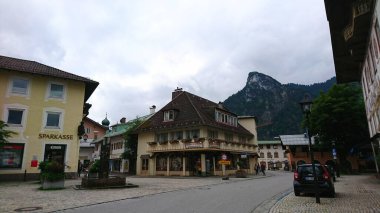 Oberammergau, Almanya - 6.14.2018: Geleneksel Bavyera mimarisi ve dağ sırasının bir zemininin yer aldığı büyüleyici sokak manzarası bulutlu bir gökyüzü altında