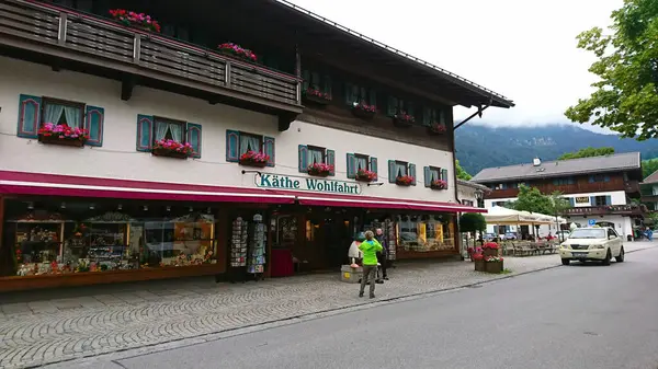 Oberammergau, Almanya - 6.14.2018: Tipik bir Bavyera dükkânı, Kathe Wohlfahrt, sisli dağların arka planına karşı canlı çiçeklerle geleneksel hediyeler sergiliyor.