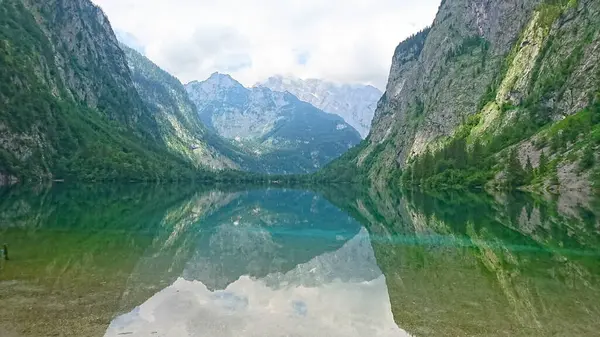 Berchtesgaden, Almanya - 6.16.2018: Konigssee 'nin sakin manzarası dramatik bulutların altındaki dağları yansıtıyor, doğada sakin bir atmosfer yaratıyor