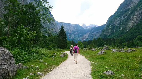 Berchtesgaden, Almanya - 6.16.2018: Berchtesgaden Dağları ve Bavyera Alpleri 'nde bulutlu bir gökyüzü tarafından çerçevelenmiş yemyeşil ve kayalık arazide dolambaçlı bir yolda yürüyen yürüyüşçüler