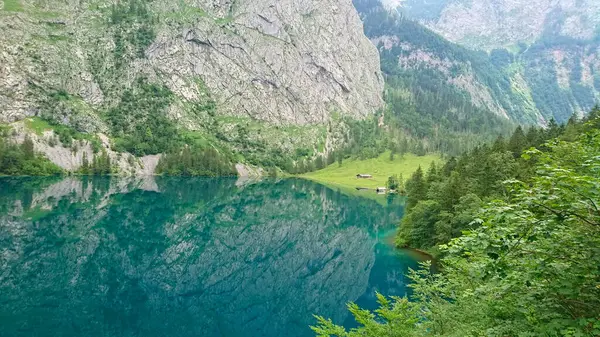 Berchtesgaden, Almanya - 6.16.2018: Berchtesgaden: Berchtesgaden Dağları ve yeşillikleri yansıtan sakin Obersee, kıyıda yemyeşil ormanlarla çevrili küçük bir kulübe