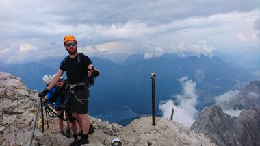 Zugspitze, Almanya - 6.17.2018: Zugspitze zirvesinde duran tırmanışçılar, dramatik dağ manzaraları ve bulutlu gökyüzü maceralı bir atmosfer yaratıyor