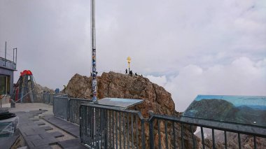 Zugspitze, Almanya - 6.17.2018: Zugspitze 'deki zirve haçı yakınlarında toplanan turistler, alp bulutları altında Bavyera Alplerinin nefes kesici yüksekliklerini gözler önüne seriyor