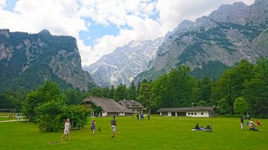 Konigssee, Almanya - 6.16.2018: Aileler, yüksek dağlar ve bulutlu gökyüzü ile çevrili yemyeşil bir çayırda dinlenme faaliyetlerinin keyfini çıkarıyorlar