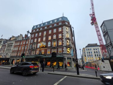 Londra, İngiltere - 1.18.2025: Piccadilly 'deki ikonik Fortnum ve Mason mağazası, bulutlu bir gökyüzü altında akşam trafiği ve yayalar arasında 2025 rakamını ön cephesinde sergiliyor