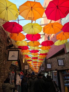 Londra, İngiltere - 11 Ocak 2025: Canlı sarı, turuncu ve kırmızı şemsiyeler, popüler Camden Market 'in dar tuğlalı sokaklarını keşfeden yayaların üzerinde renkli bir tepe örtüsü oluşturur.