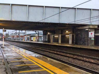St Albans, İngiltere - Ocak 12025: St. Albans Şehir İstasyonu 'nda bulutlu bir günde, raylı, sarı dokunmatik kaldırımlı ve üstten köprü yapısı olan boş, ıslak bir tren istasyonu