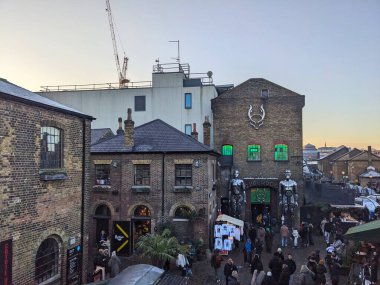 Londra, İngiltere - 11 Ocak 2025: Camden Market 'teki kalabalık göz gezdirme dükkanlarının ve market tezgahlarının yüksek açılı görüntüsü, tarihi tuğla binalar akşam karanlığında canlı bir kentsel atmosfer yaratıyor