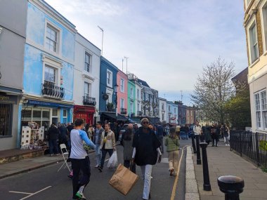 Londra, İngiltere - 3.29.2025: Portobello Yolu boyunca yürüyen yayalar, Notting Hill bölgesinde canlı pazarı ile tanınan renkli teraslı evler ve dükkanlarla