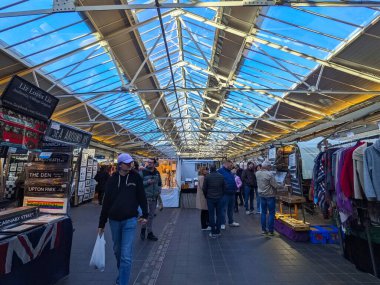 Londra, İngiltere - 2 Şubat 2025: Alışverişçiler tarihi Greenwich Pazarı 'nın güneşli cam çatısı altında antika tabelalar ve giysiler satan tezgahları keşfederek canlı bir şehir manzarası yarattılar