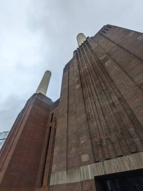 Londra, İngiltere - 2.9.2025: İkonik Battersea Enerji İstasyonları 'nın alçak açılı görünümü tuğla cephe ve gri gökyüzüne karşı belirgin bacalar, onun görkemli Art Deco endüstriyel tasarımı vurgulanıyor