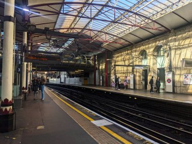 Londra, İngiltere - 3.29.2025: Yolcular, tarihi mimari ve Elizabeth serisi gibi modern ulaşım bağlantılarının yer aldığı önemli bir Londra kavşağı olan Farringdon istasyonunda güneşli platformlarda bekliyorlar