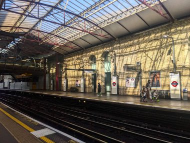 Londra, İngiltere - 29 Mart 2025: Yolcular Farringdon İstasyonu 'ndaki güneşli bir platformda bekliyorlar, Londra Yeraltı Ağı' nın bir parçası olan cam çatıya güneş ışığı yansıyor.