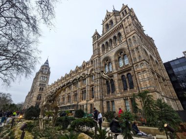 Londra, İngiltere - 2.15.2025: Ziyaretçiler, Güney Kensington 'da bir kış günü, Güney Kensington' da bulutlu bir gökyüzü altında, Romanesk Doğal Tarih Müzeleri cephesine ve Diplodocus iskelet kopyasına hayran kaldılar.