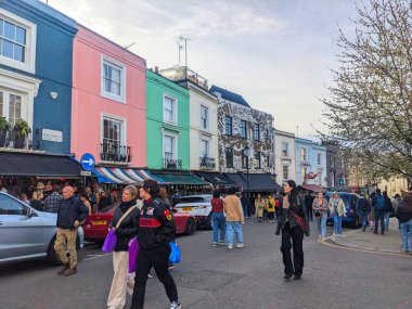 Londra, İngiltere - 3.29.2025: Portobello Yolu boyunca yürüyen yayalar, Notting Hill 'deki renkli teraslı evleri ve canlı pazar atmosferiyle bulutlu bir gökyüzü altında